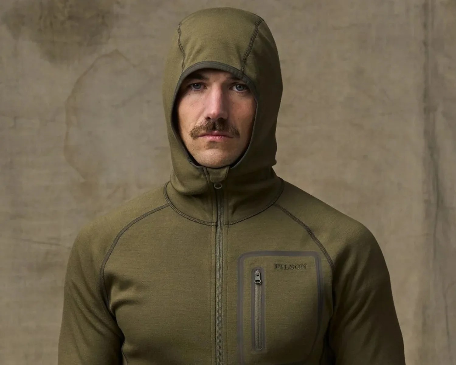 Man wearing an olive green zip-up hoodie with a chest pocket and "Filson" logo.