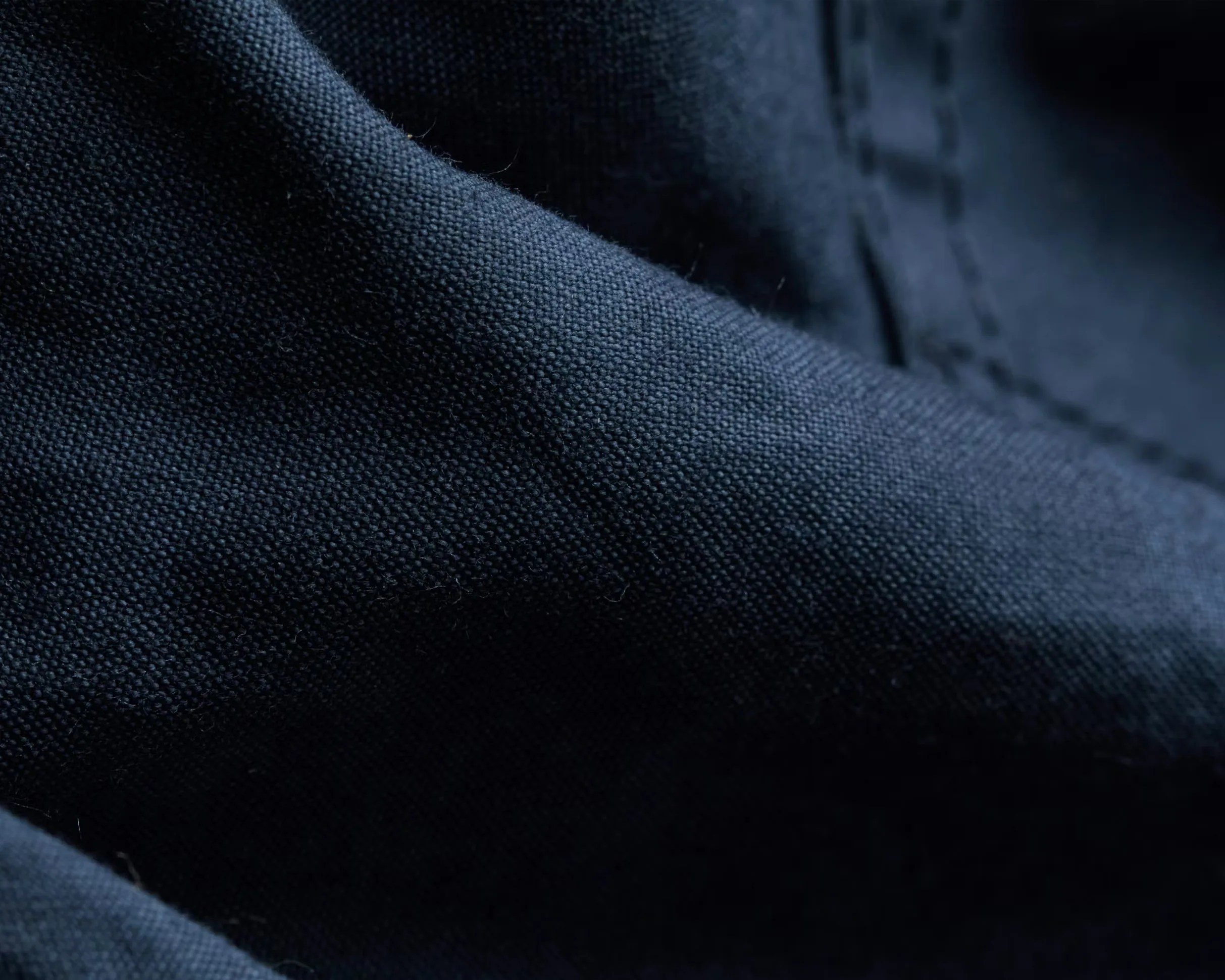 Close-up of dark blue textured fabric with visible weave and stitching.
