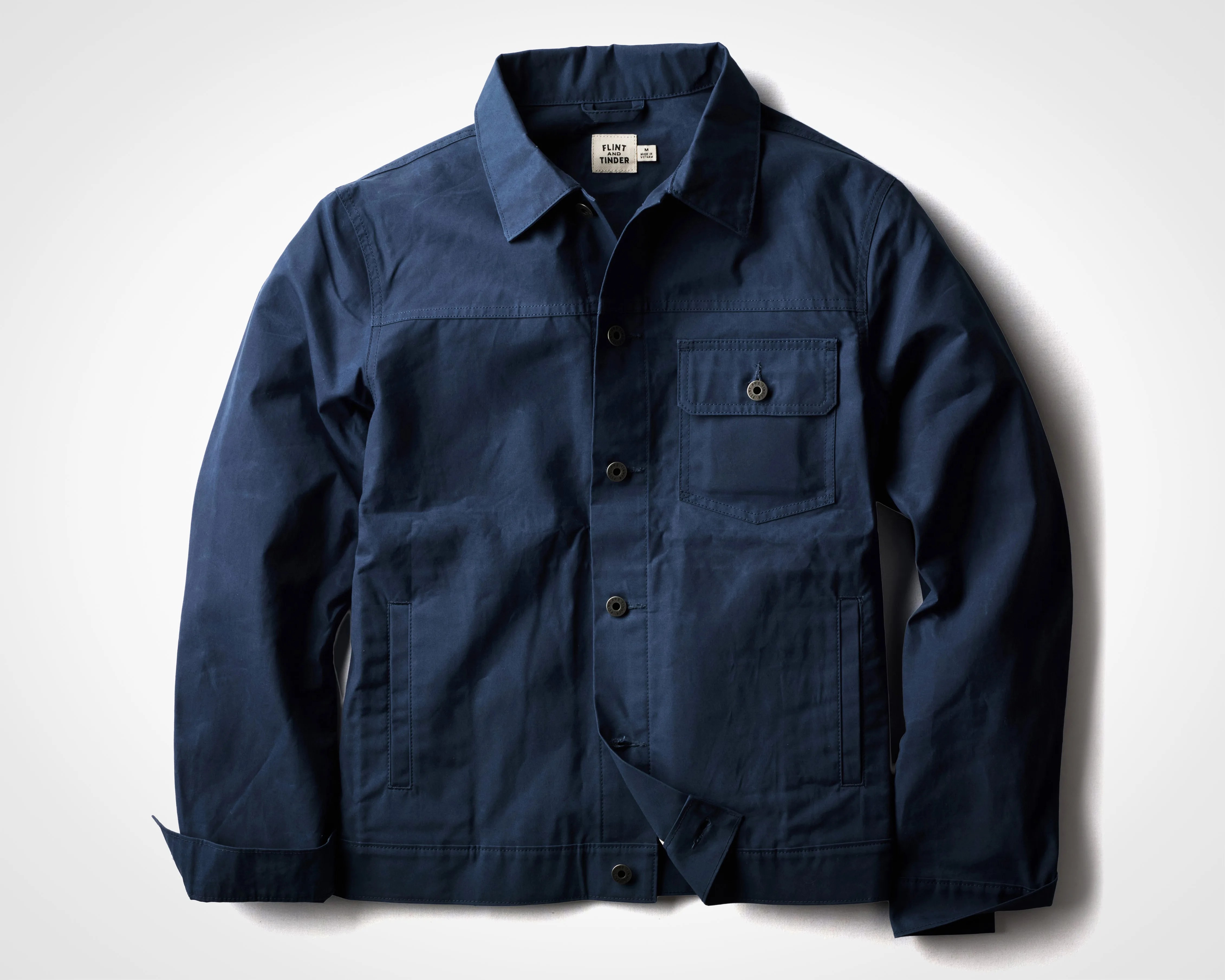 Navy blue button-up jacket with a chest pocket and two side pockets laid flat on a white surface.