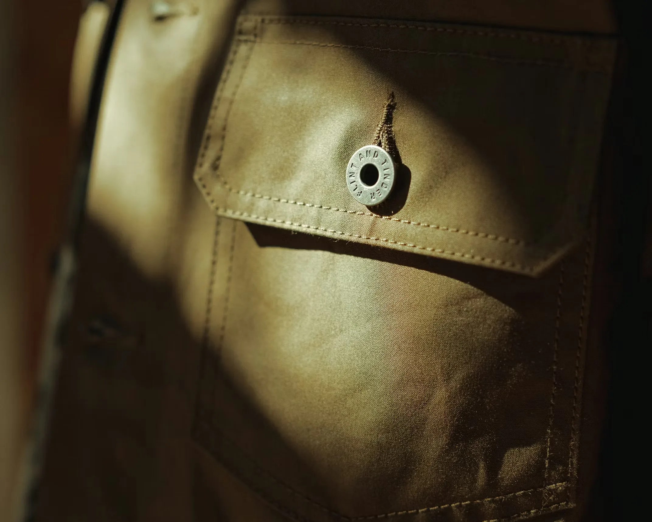 Close-up of a brown fabric pocket with a metal button engraved "FLINT AND TINDER.