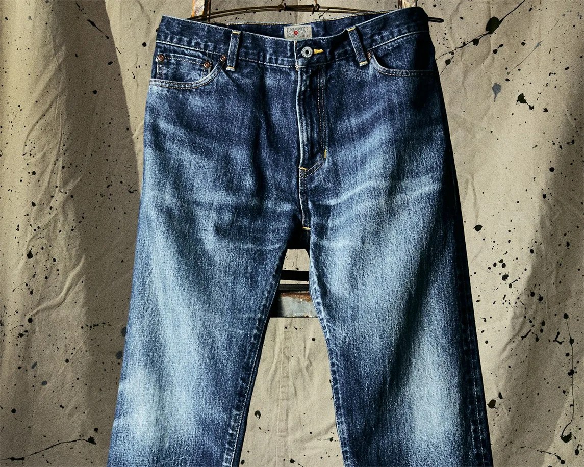 Blue faded denim jeans hanging against a beige splattered backdrop.