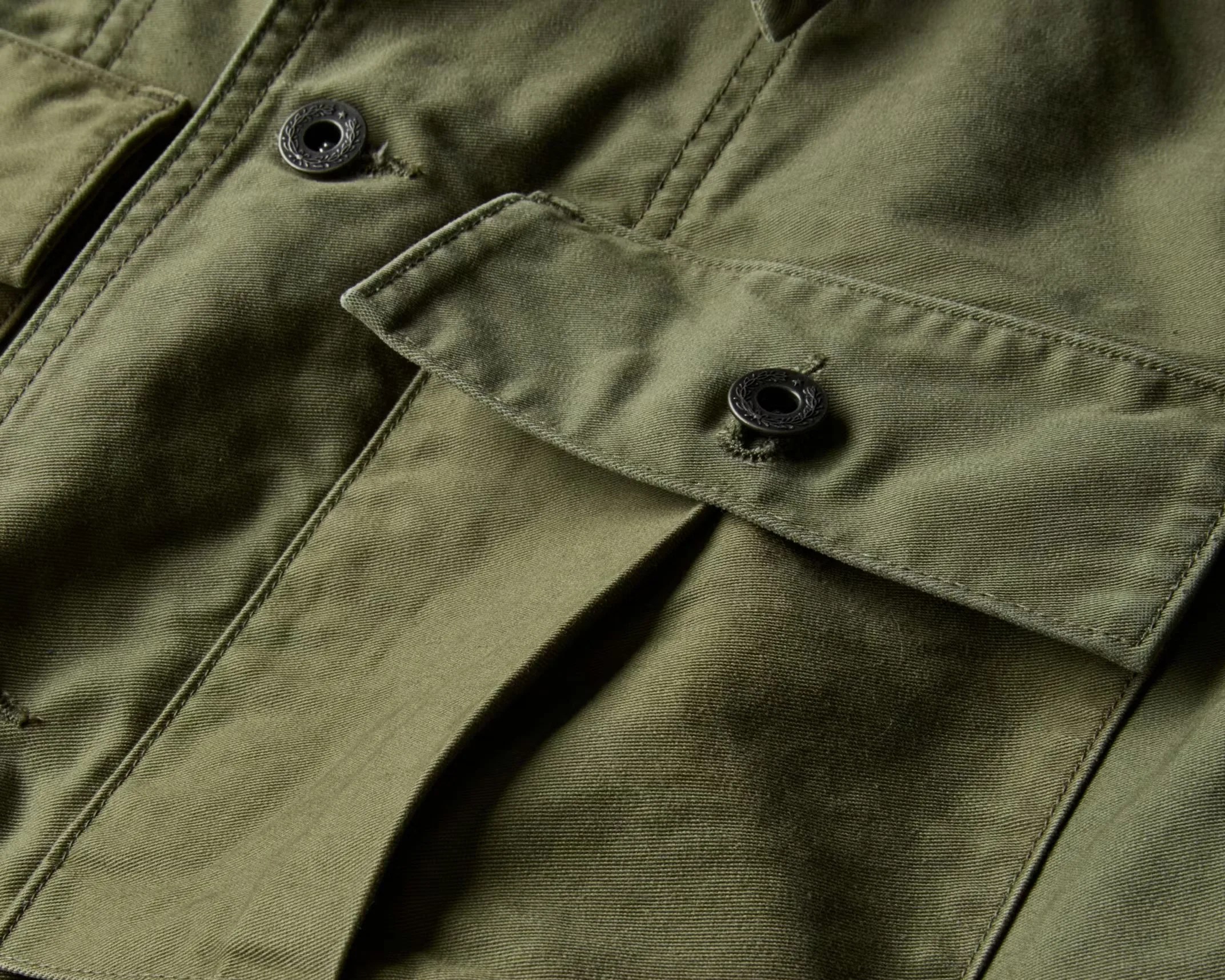 Close-up of an olive green fabric jacket pocket with a flap secured by a black button.