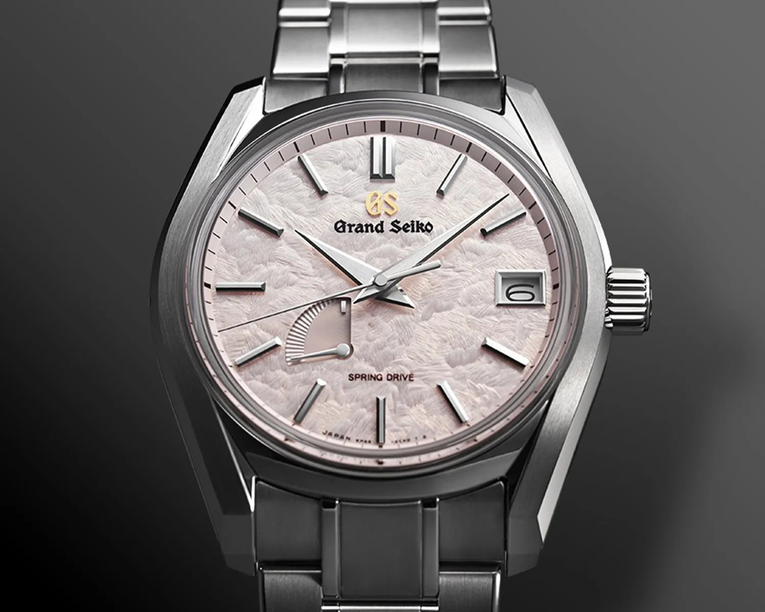 Grand Seiko stainless steel wristwatch with textured light pink dial, date window, and power reserve indicator.