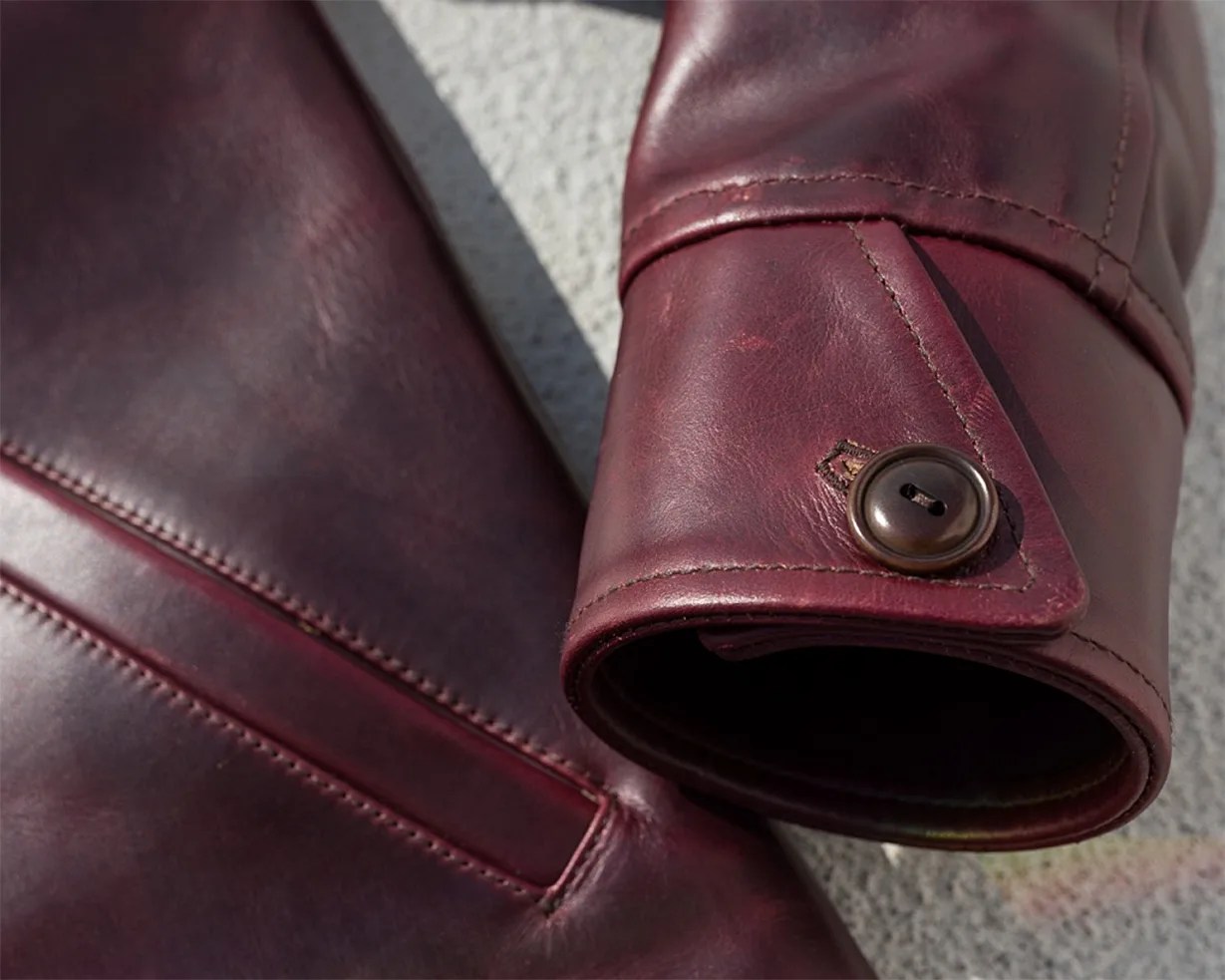 Close-up of burgundy leather jacket sleeve with a buttoned cuff detail.