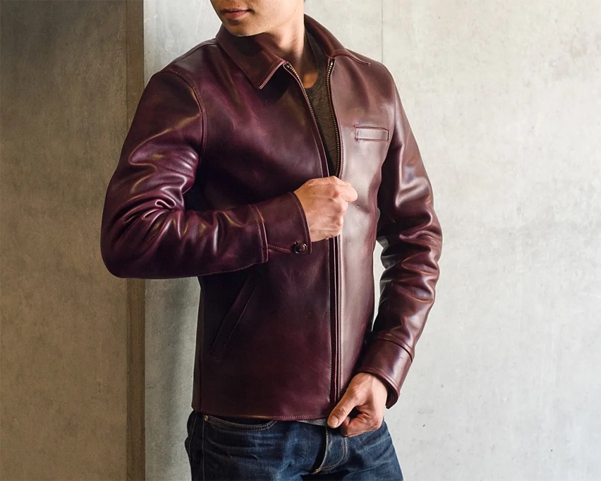 Man wearing a fitted dark brown leather jacket with a zipper and buttoned cuffs.