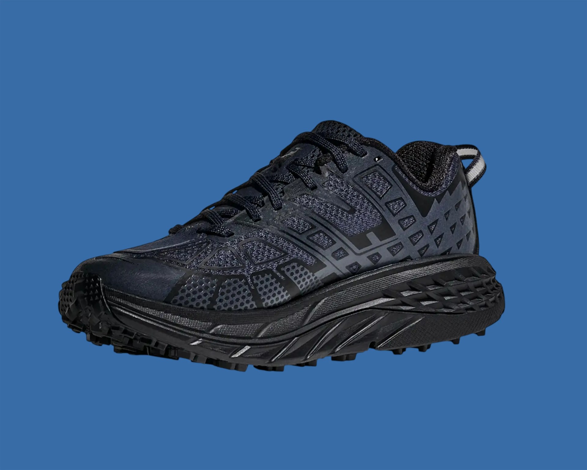 Black trail running shoe with textured sole and geometric patterned upper on blue background.