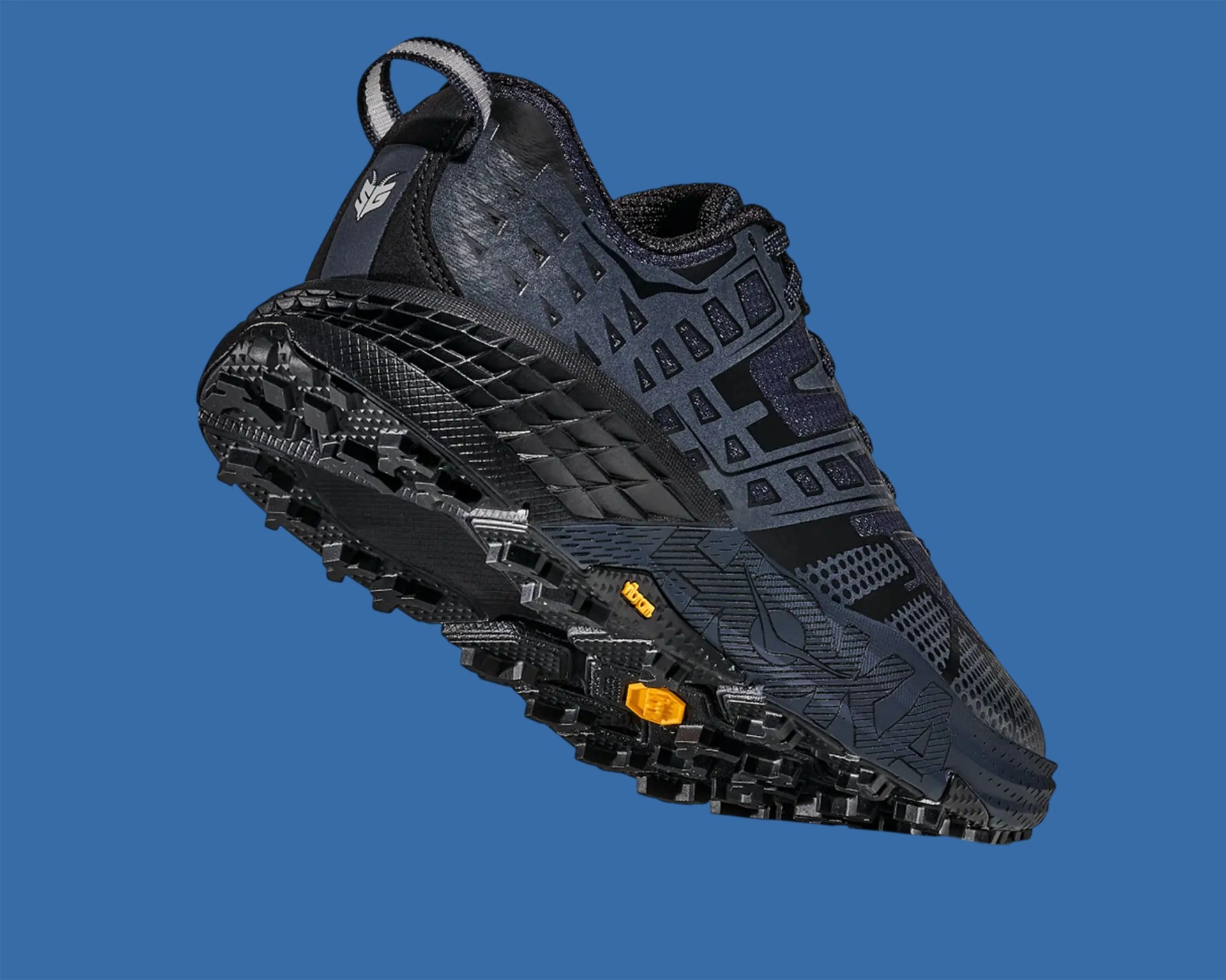 Black and dark gray trail running shoe with textured sole and pull tab on blue background.