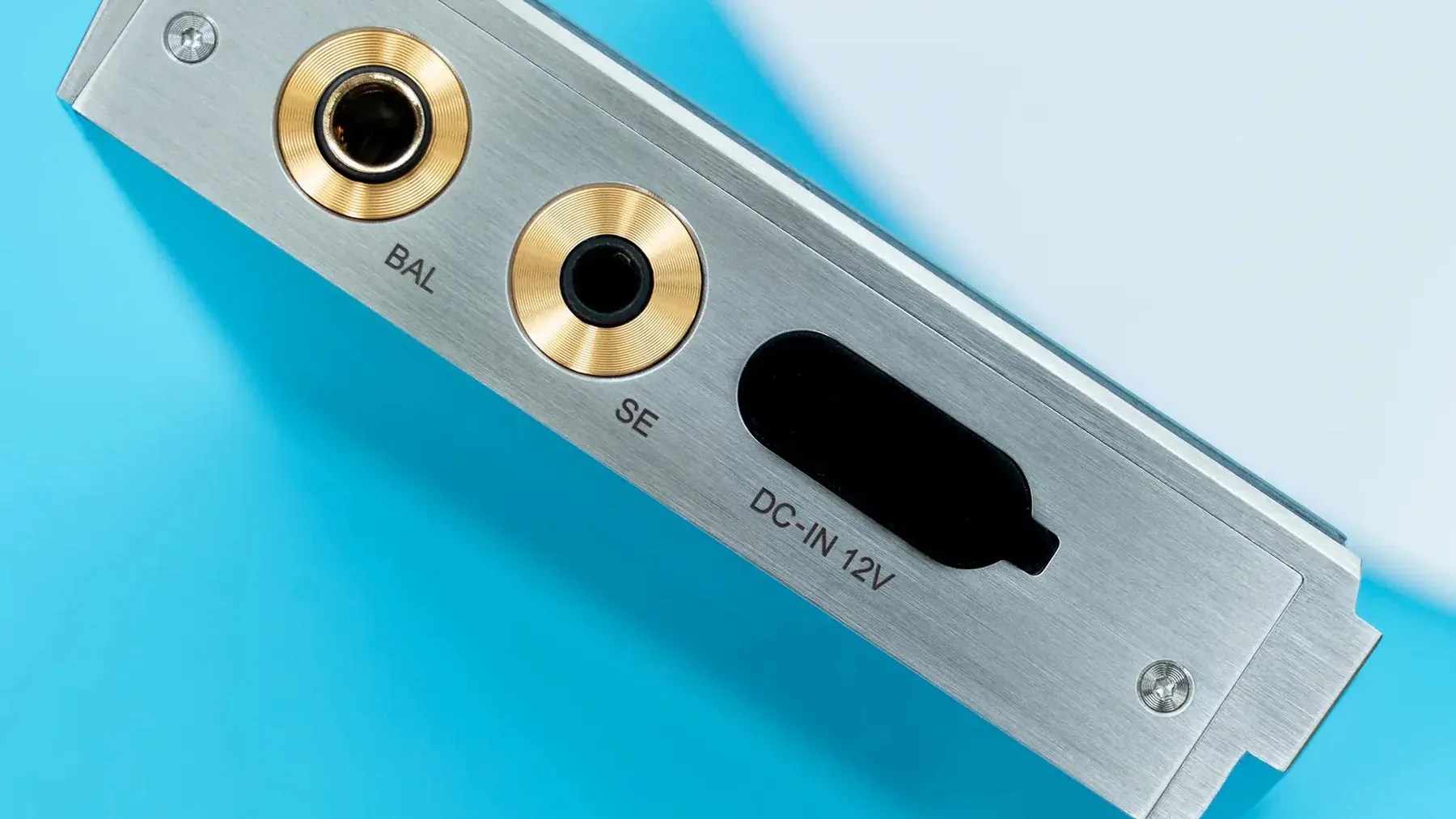 Close-up of a silver metal panel with gold-ringed BAL and SE audio jacks and a DC-IN 12V power input on a blue background.
