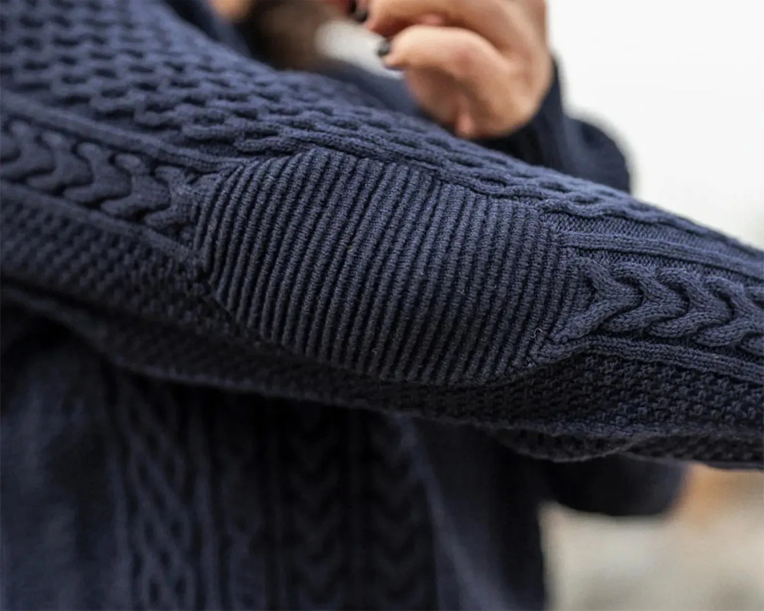 Close-up of a navy blue cable-knit sweater sleeve with a ribbed elbow patch.