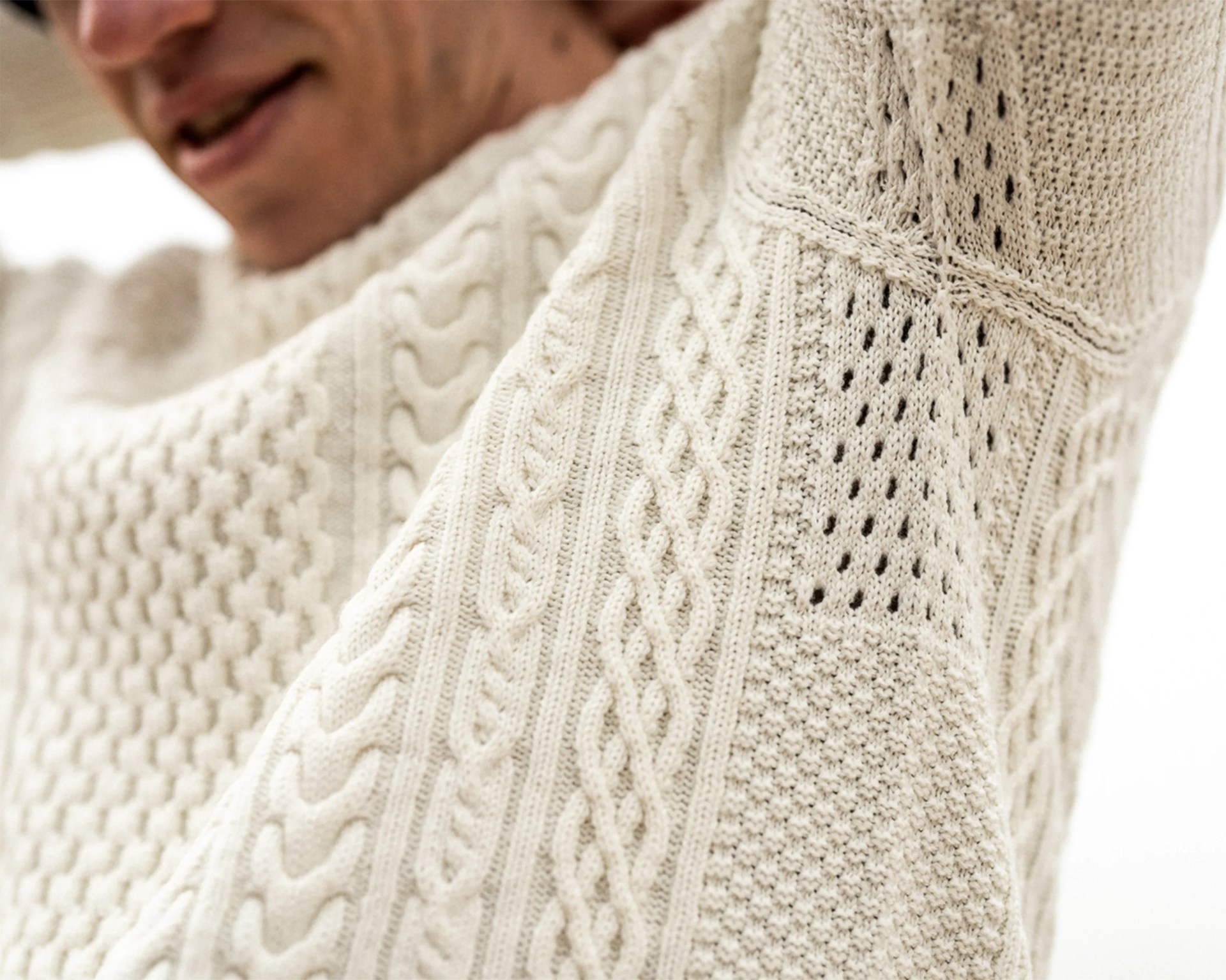 Cream-colored cable knit sweater with intricate patterns worn by a person.