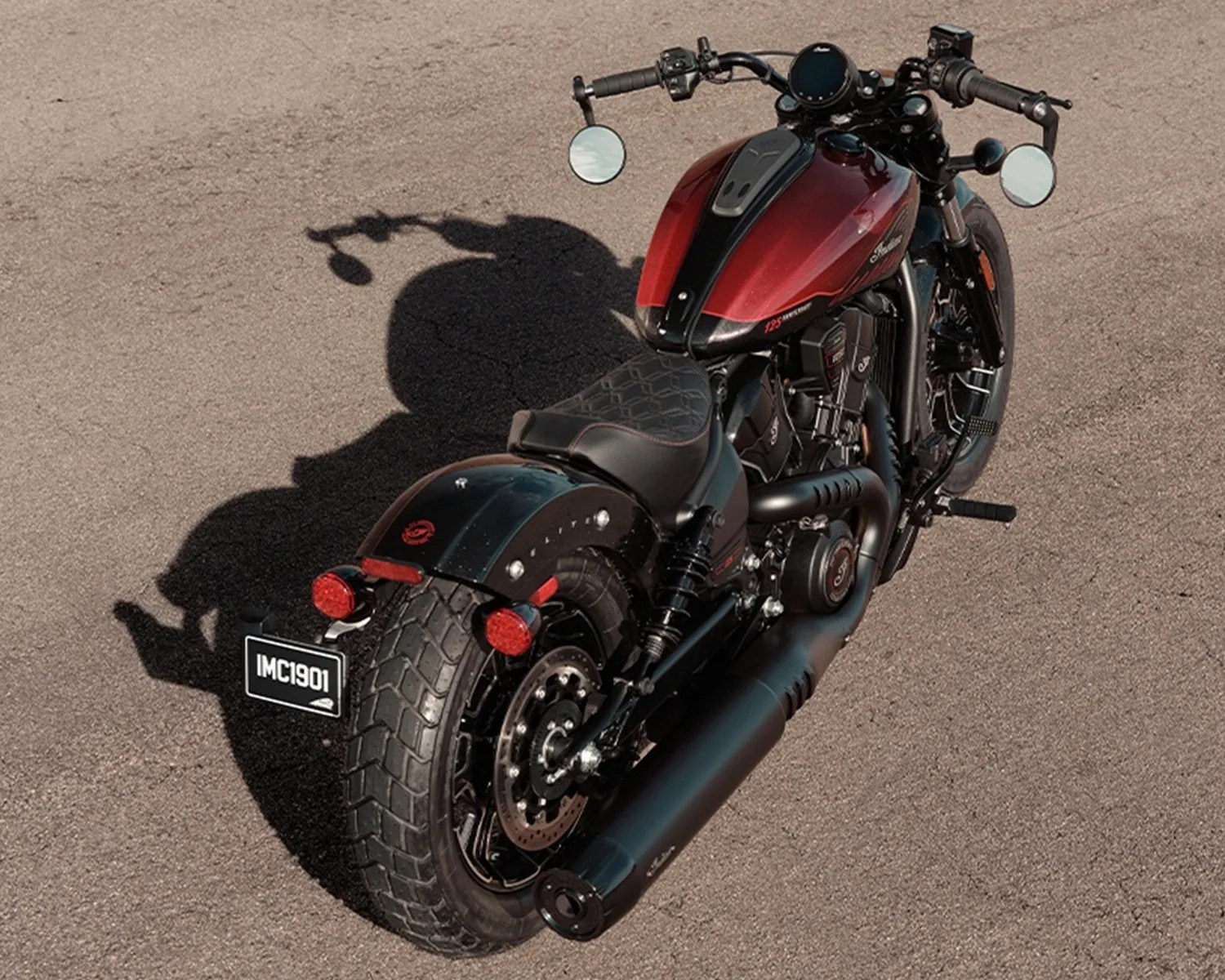 Red and black cruiser motorcycle with wide rear tire and round mirrors on asphalt.