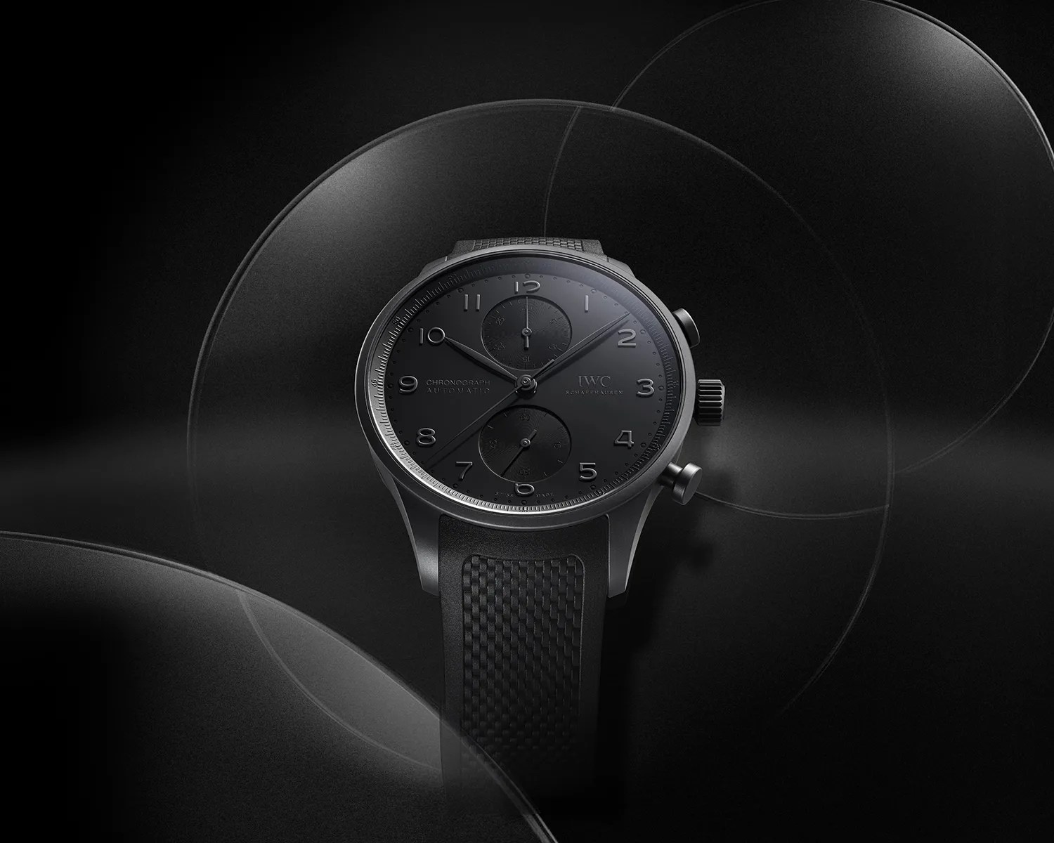 Black chronograph wristwatch with textured rubber strap and matte black dial on a dark background.