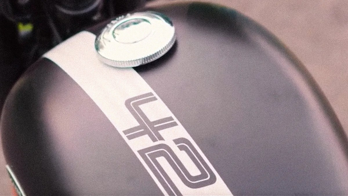 Close-up of a matte black motorcycle fuel tank with a white stripe and a silver fuel cap.
