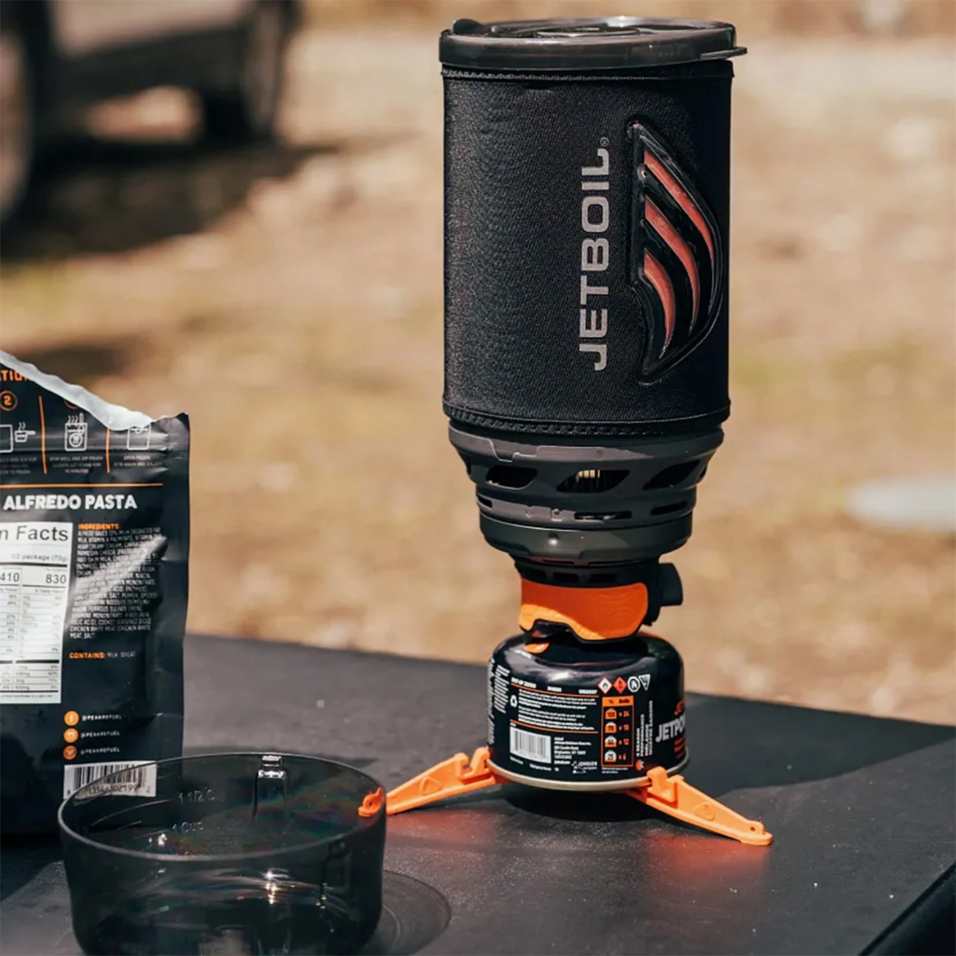Black and orange Jetboil portable camping stove with fuel canister and stabilizing legs on a table.