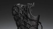 Black knitted sneaker with a unique web-like lacing system and textured sole against a dark gradient background.