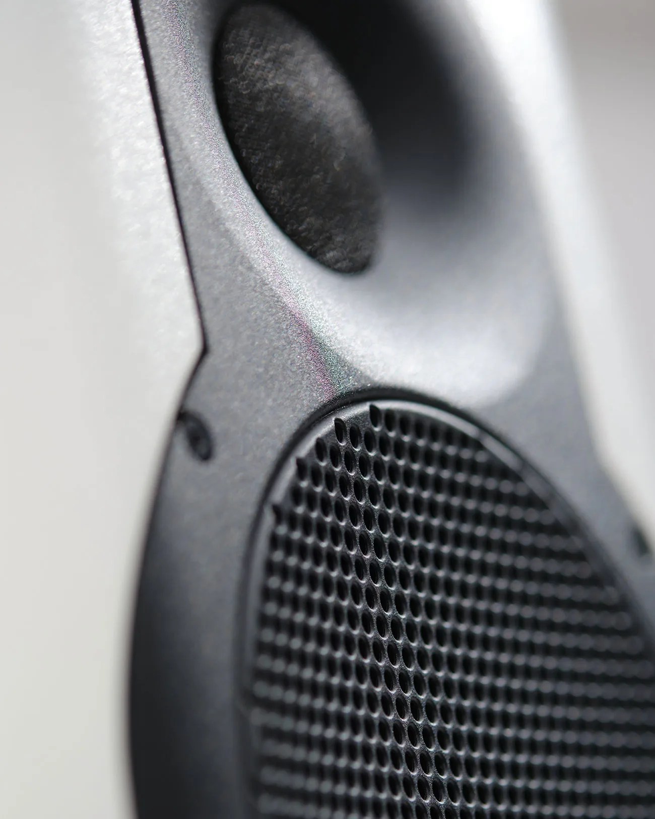 Close-up of a black speaker grille with a textured cone above it on a gray surface.