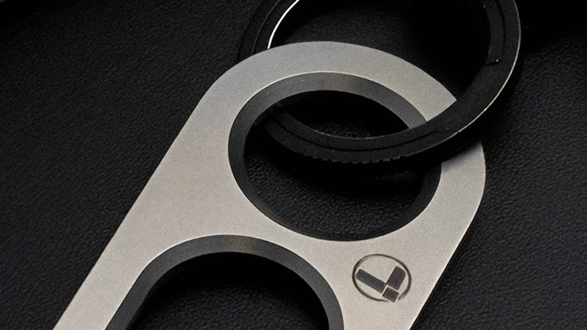 Silver metal keychain with two circular openings and a black rubber ring on a black textured surface.