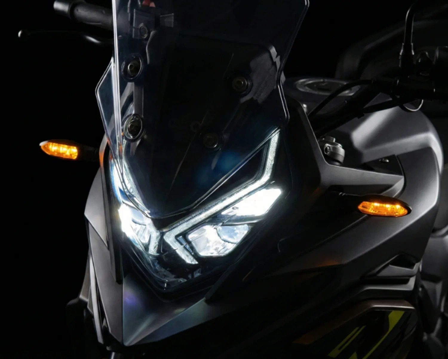 Front view of a black motorcycle with LED headlights and amber turn signals illuminated against a dark background.