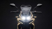 Front view of a beige motorcycle with dual headlights turned on and black rearview mirrors against a dark background.