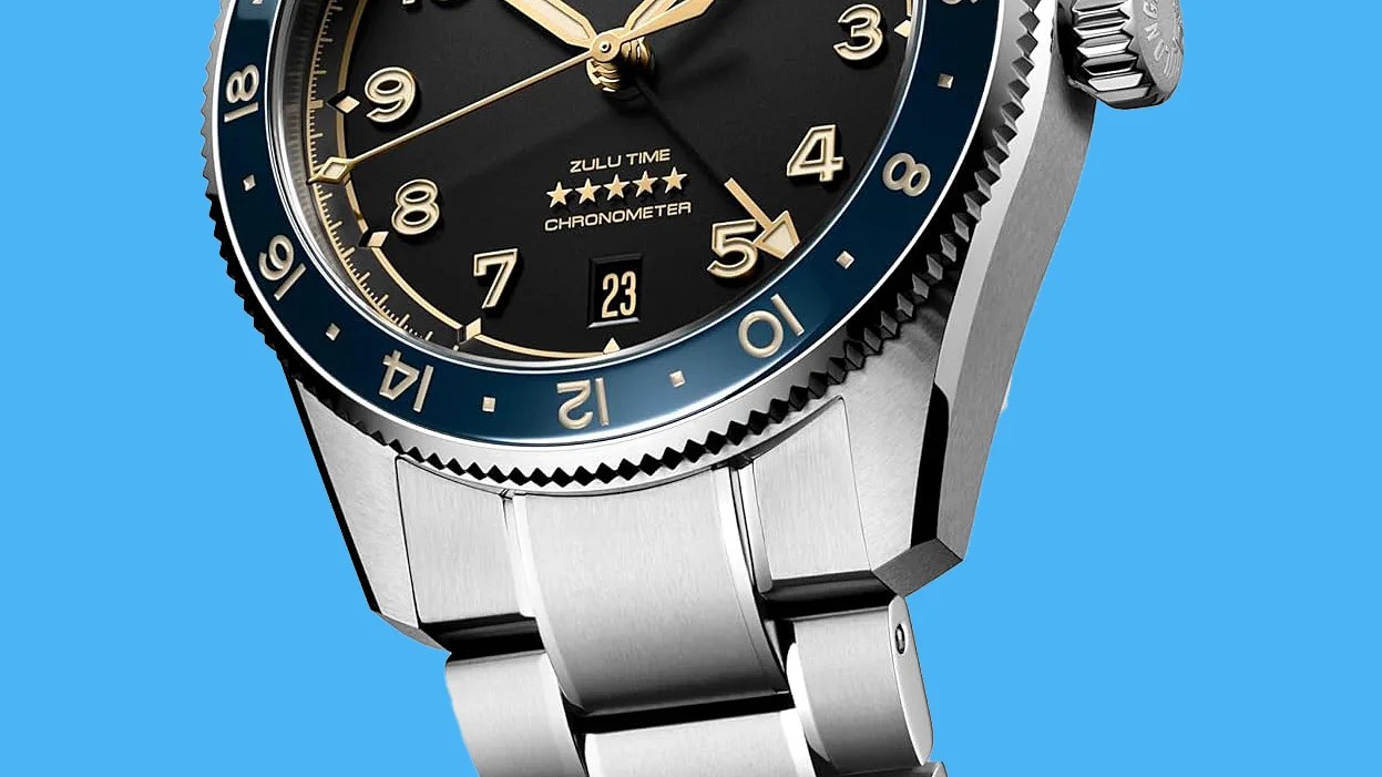 Close-up of a stainless steel wristwatch with a black dial, gold numerals, blue bezel, and date display at 6 o'clock.