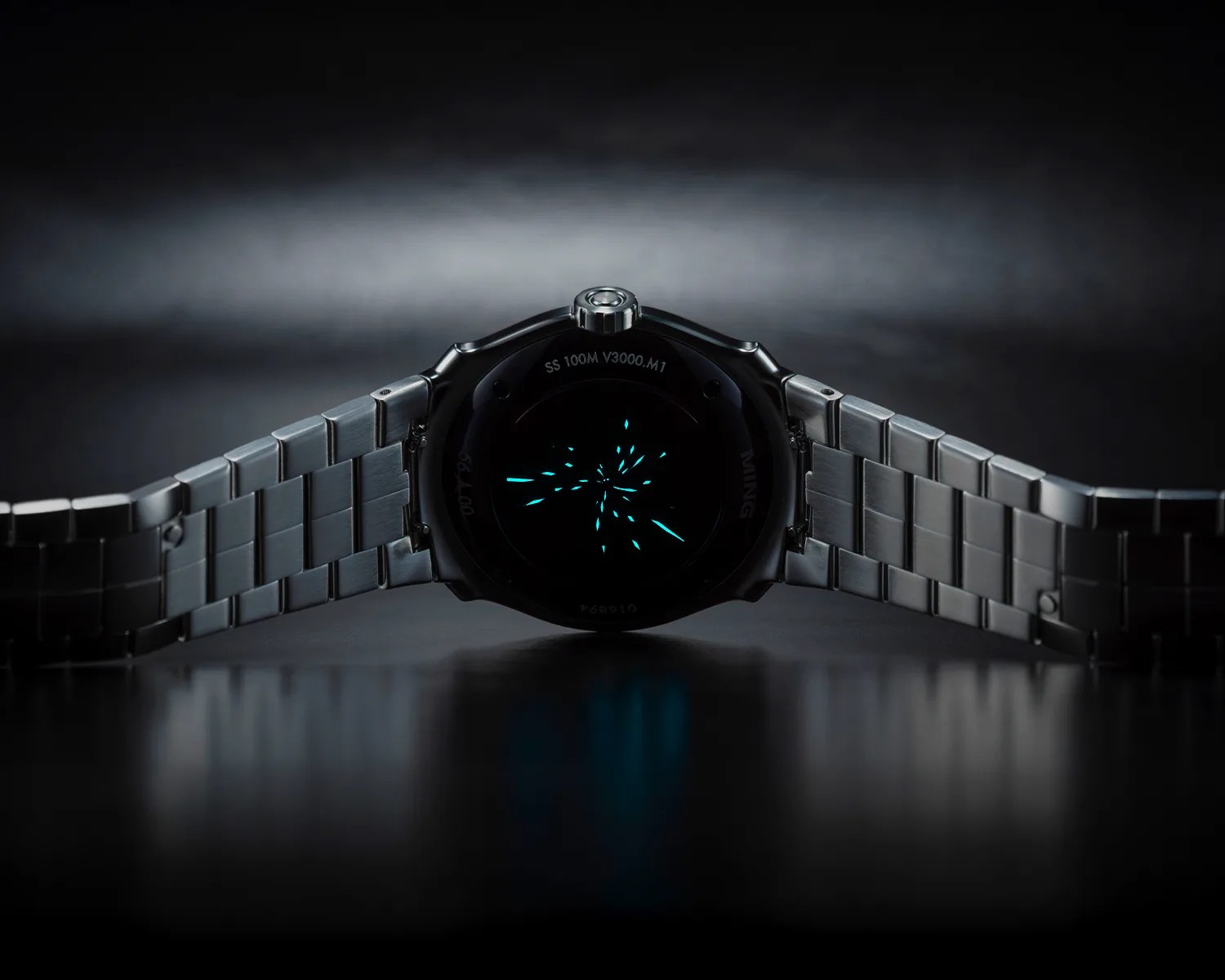 Stainless steel wristwatch with a metal link bracelet and glowing blue marks on the dark caseback.