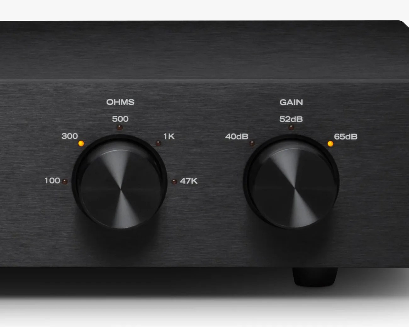 Close-up of black brushed metal audio device with two large black knobs labeled "OHMS" and "GAIN" with orange indicator lights.