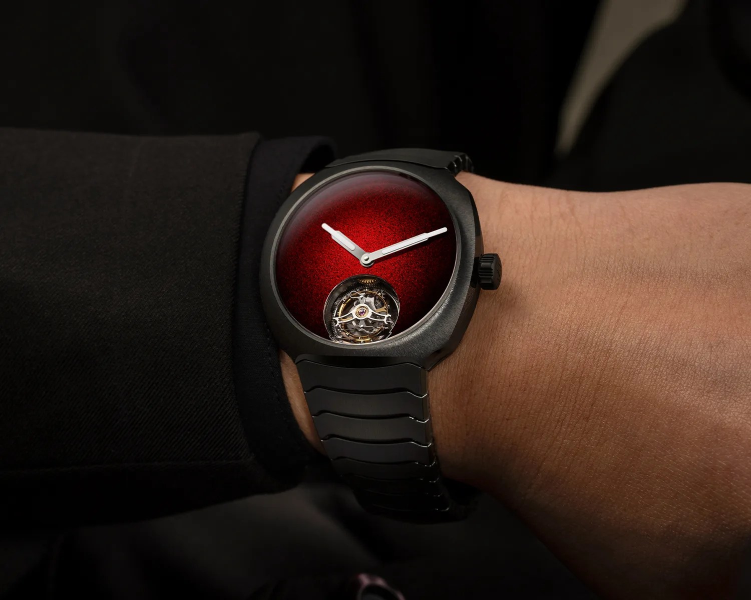 Black wristwatch with a deep red textured dial and visible tourbillon mechanism worn on a wrist.