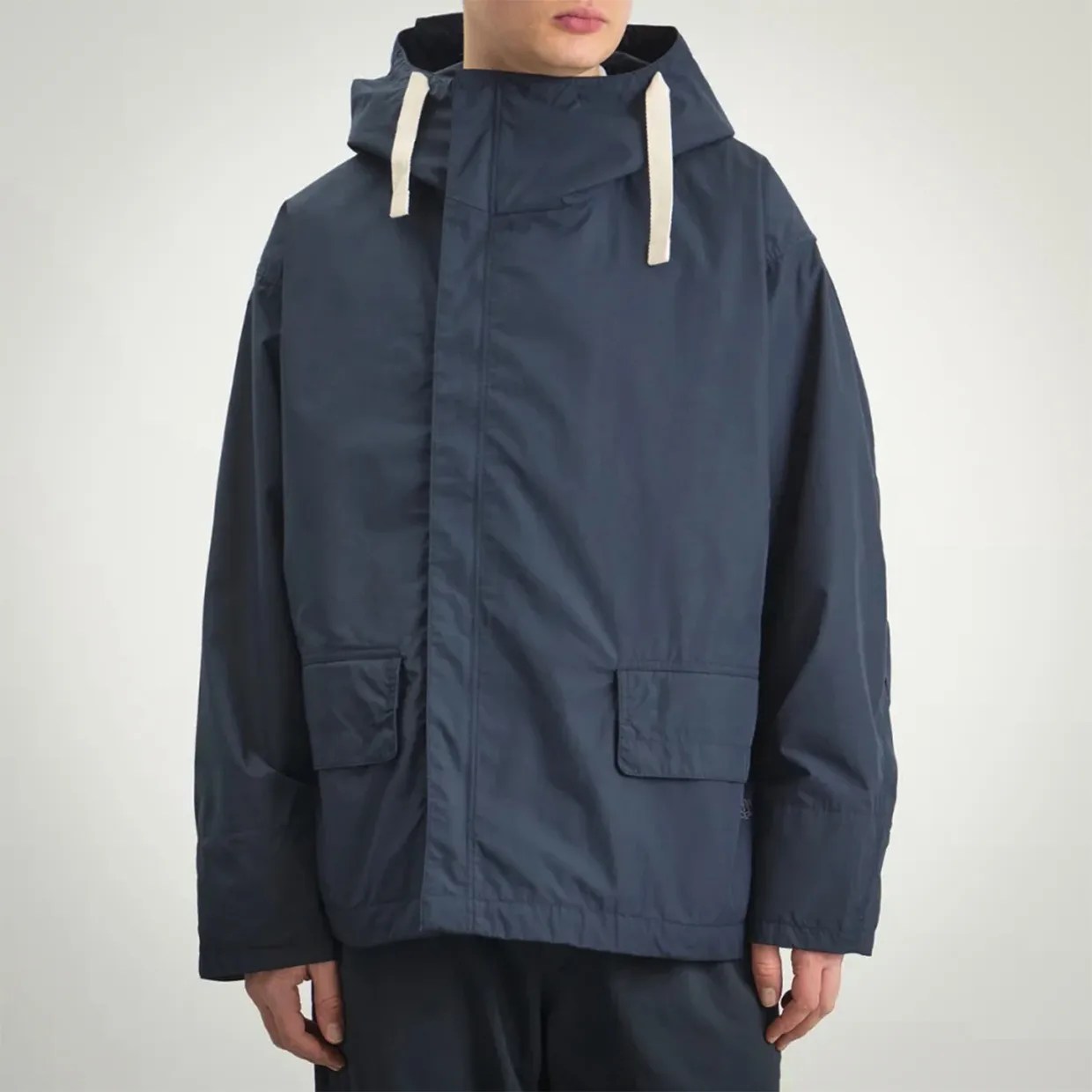 Navy blue hooded jacket with front flap pockets and white drawstrings worn by a person.