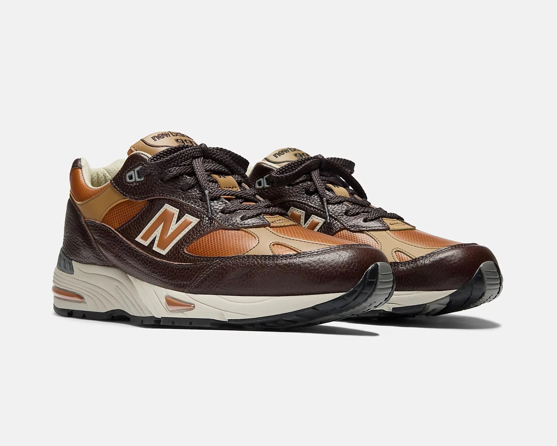 Pair of brown and tan New Balance sneakers with black laces and white midsoles on a white background.