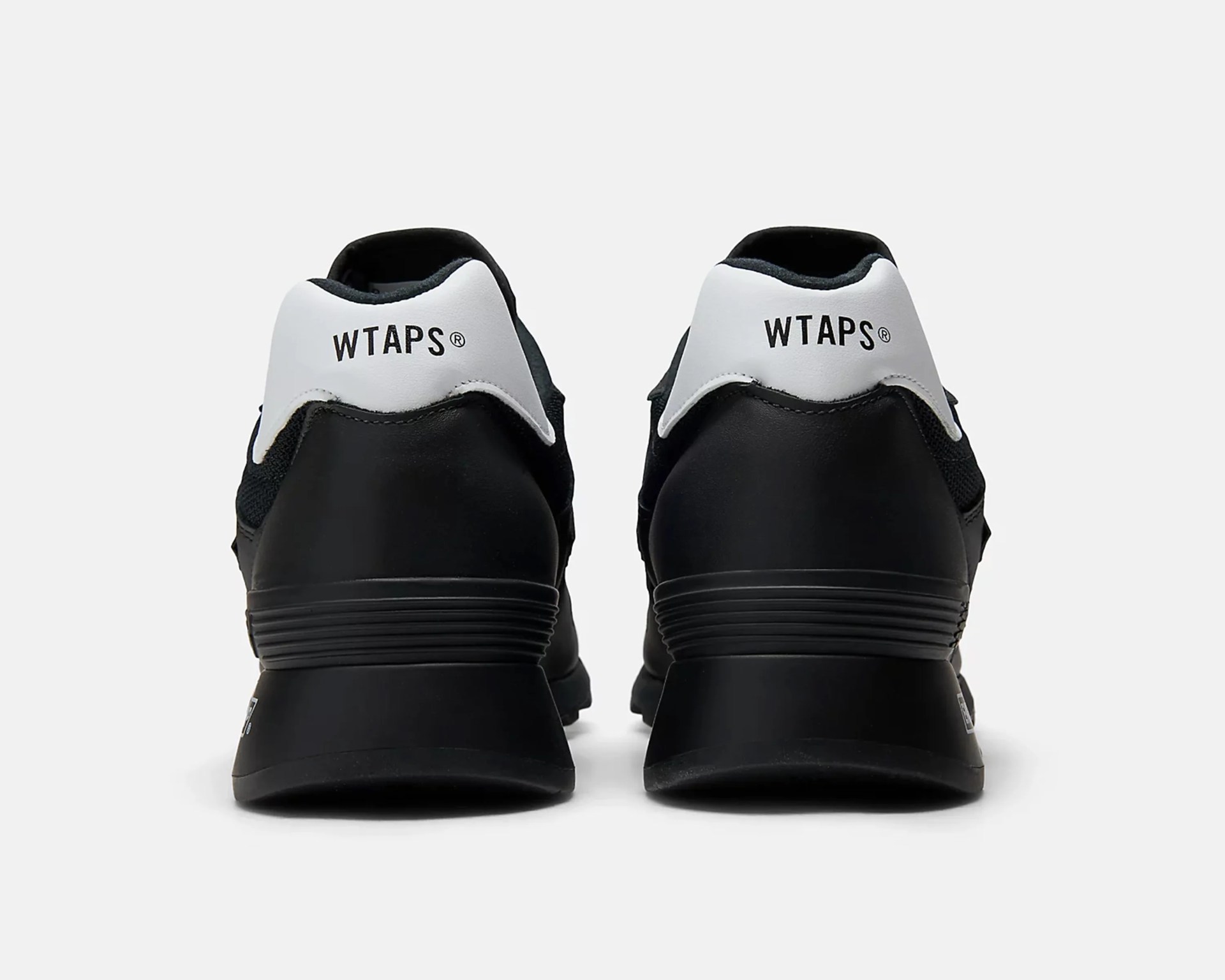 Pair of black sneakers with white heel tabs featuring "WTAPS" branding, shown from the back.