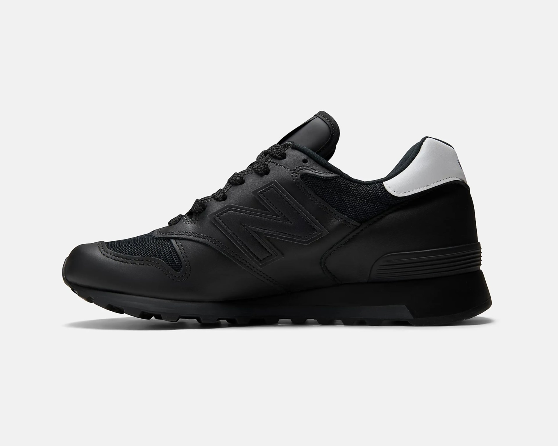Black New Balance sneaker with mesh and leather upper and white heel tab, shown in side profile.