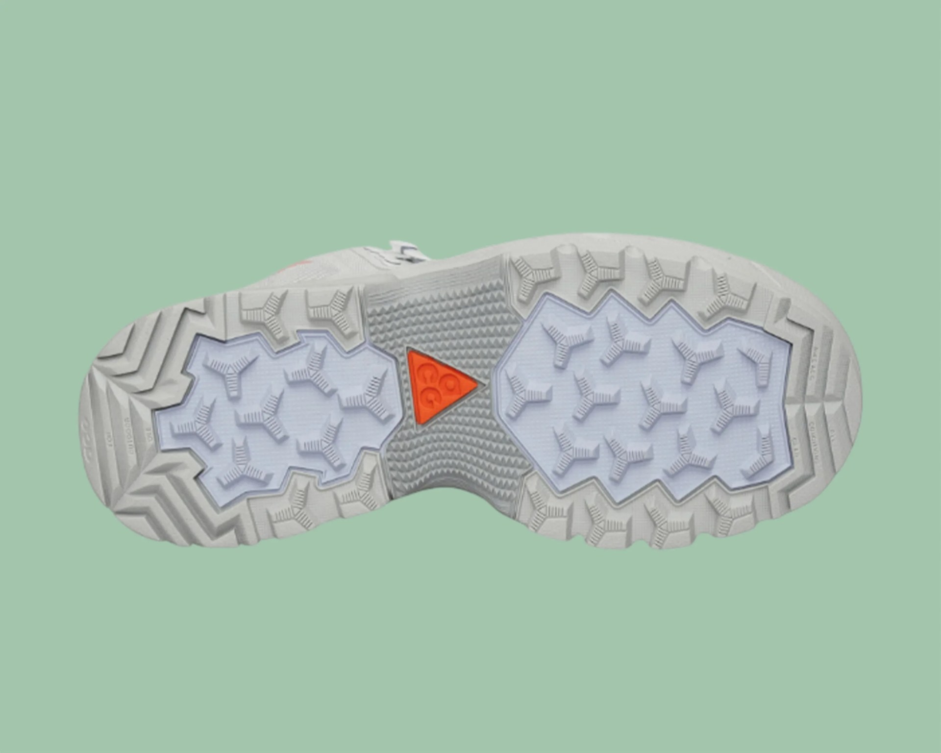 Light gray shoe sole with white and orange traction pads on a green background.