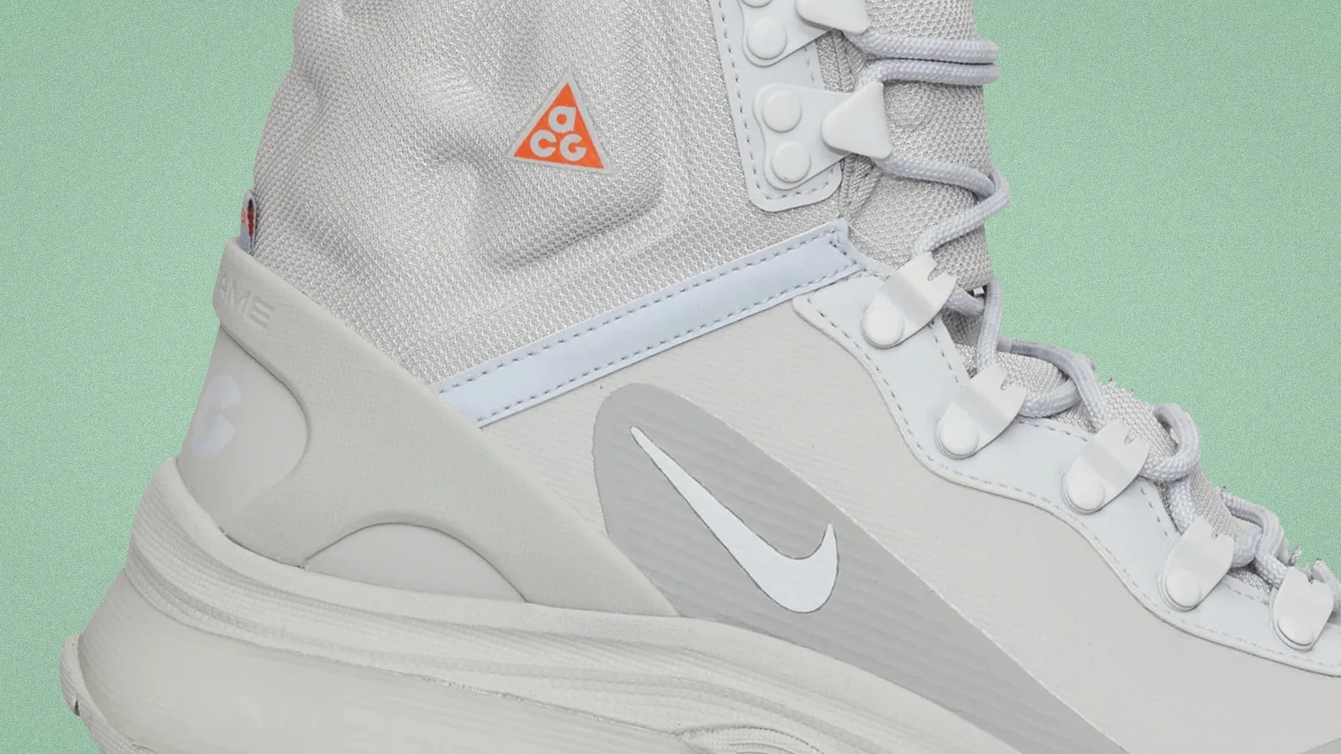 Close-up of a light gray Nike ACG hiking boot with white laces and an orange ACG logo on the side.