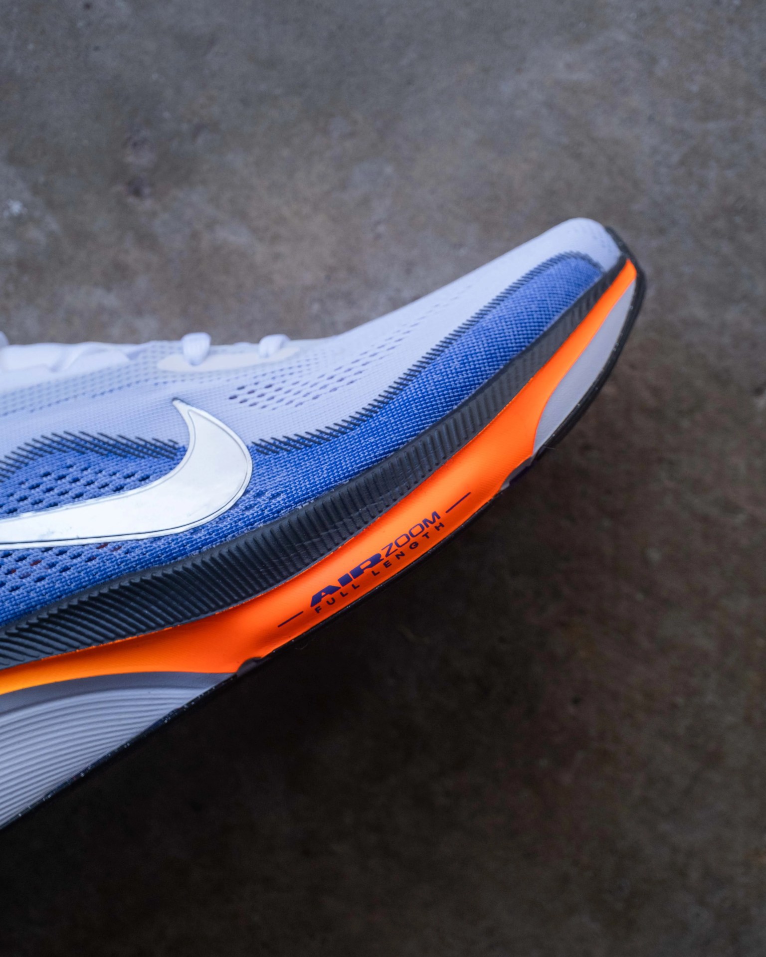 White and blue Nike Air Zoom running shoe with orange sole detail on a concrete floor.