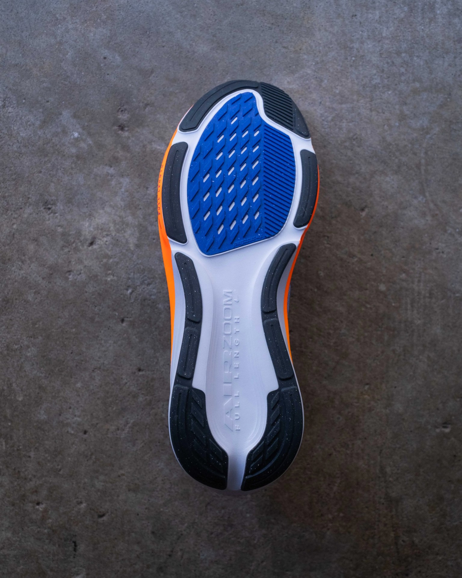 Sole of an orange running shoe with black, blue, and white rubber tread on a concrete floor.