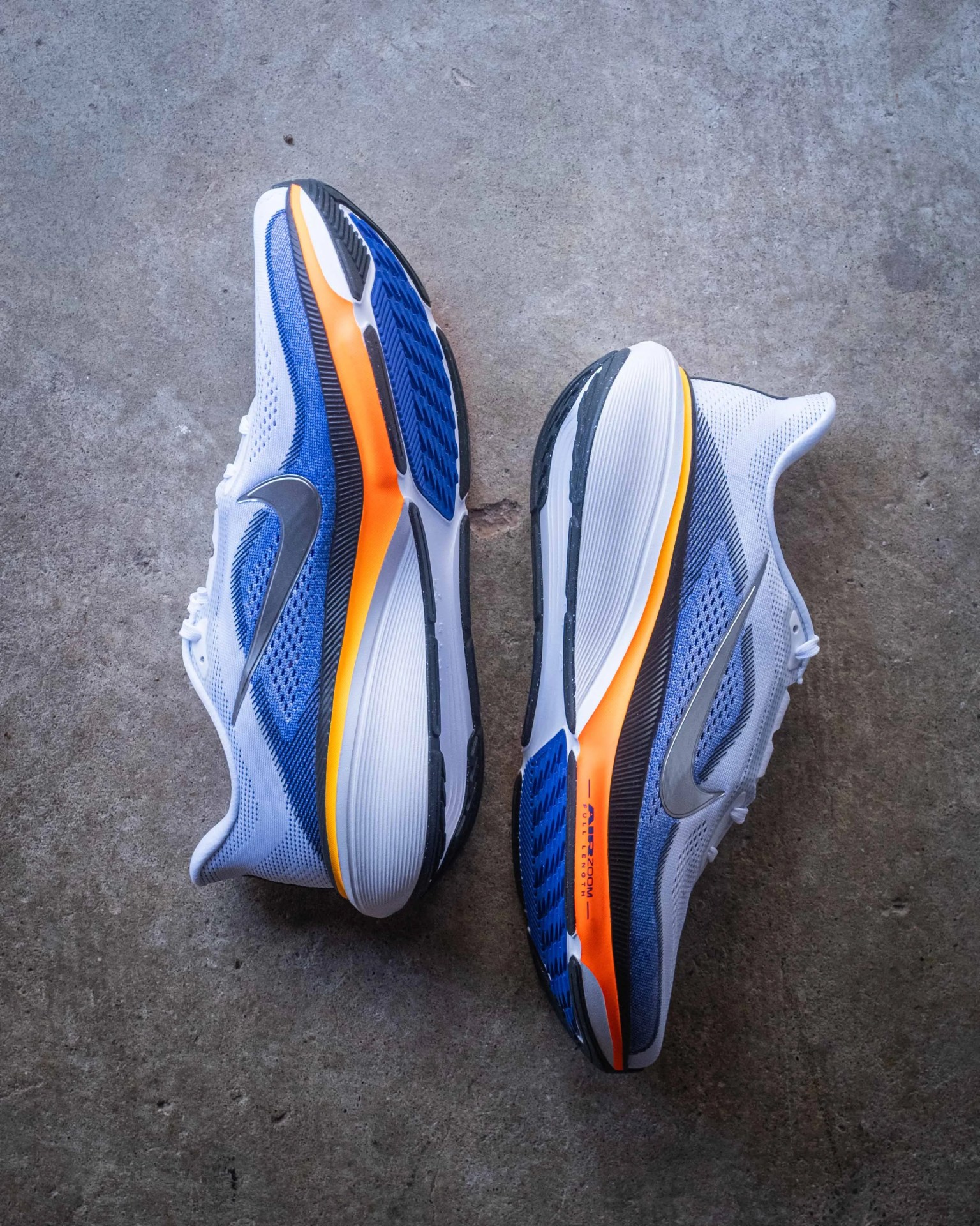Pair of white and blue Nike running shoes with orange and black soles on a concrete floor.
