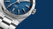 Close-up of a silver stainless steel watch with a textured blue dial and silver hour markers on a blue background.
