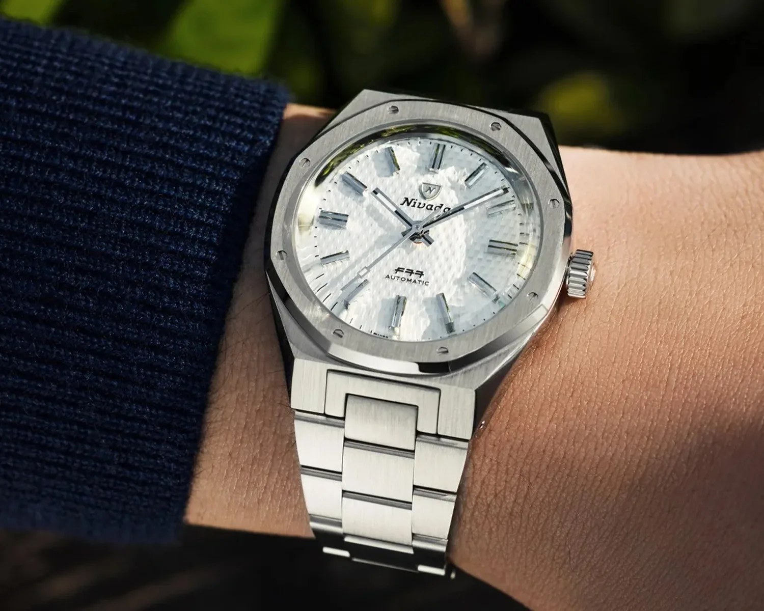 Silver stainless steel wristwatch with a textured white dial and metal bracelet worn on a wrist.