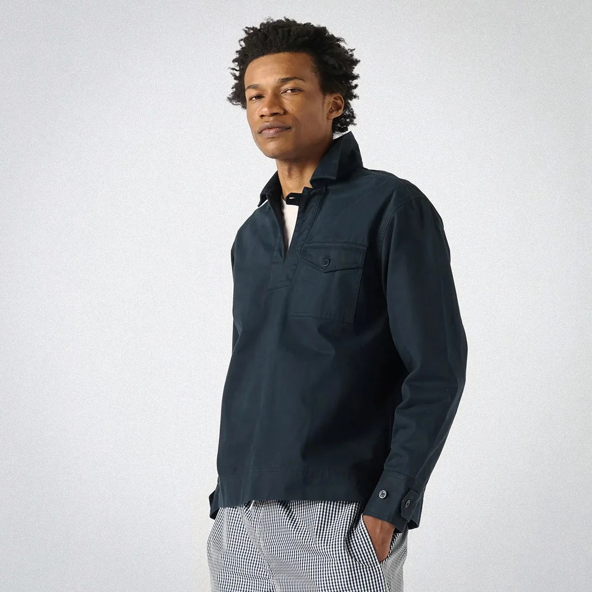 Man wearing a dark navy pullover shirt with a buttoned chest pocket and checkered pants.