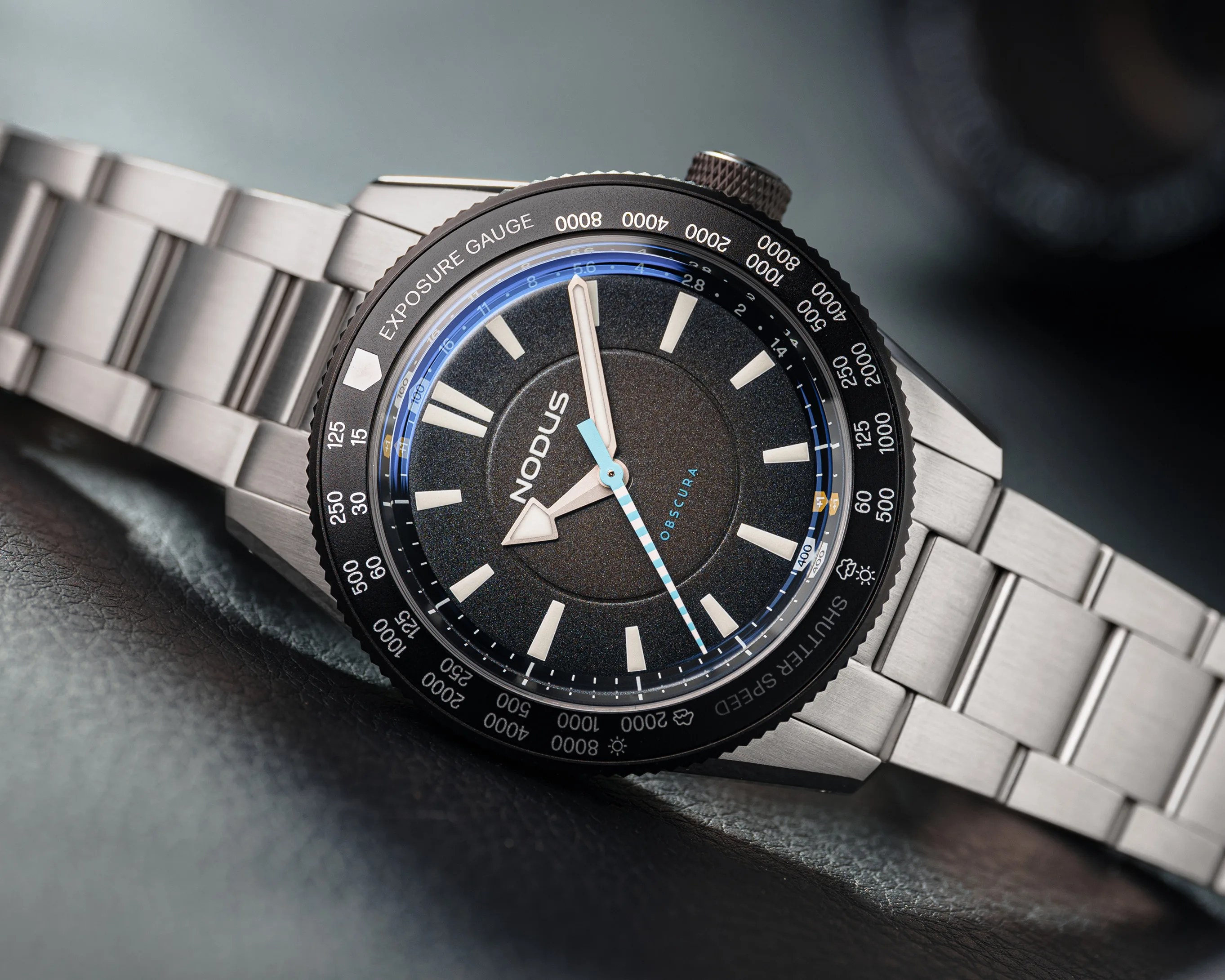 Stainless steel wristwatch with black textured dial, white hour markers, and blue-striped second hand on a metal bracelet.