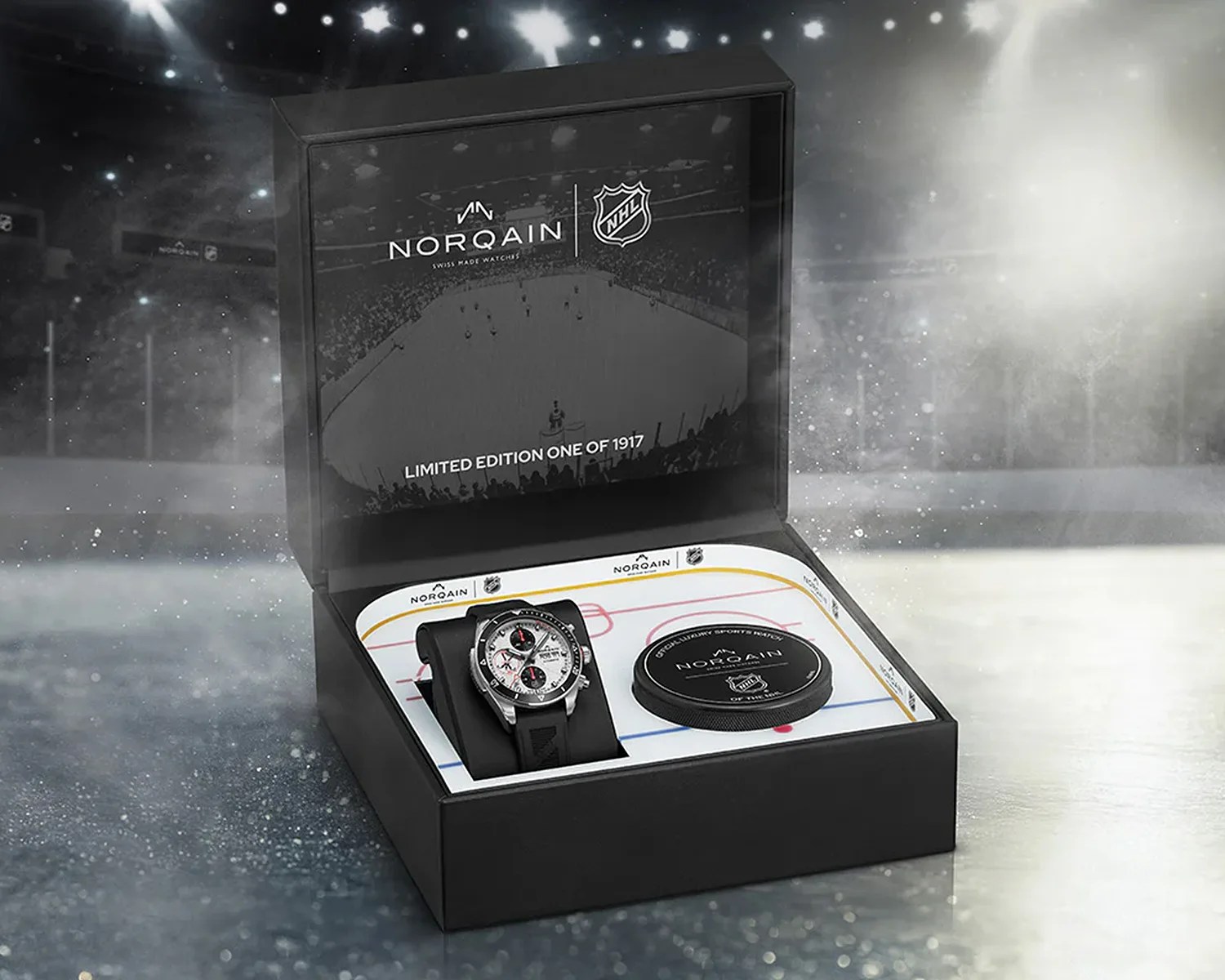Open black box containing a Norqain Swiss watch with black strap and a hockey puck on an ice rink-themed insert.