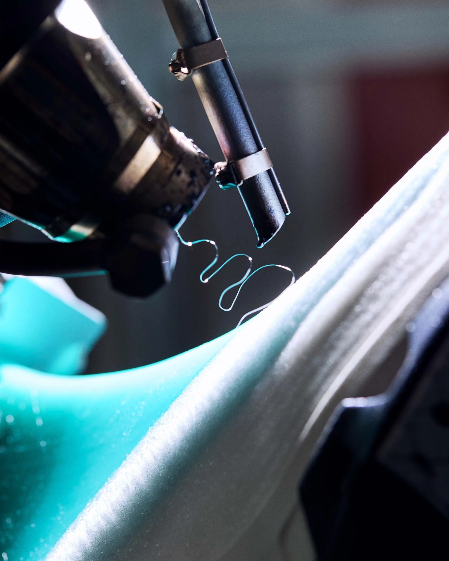 Close-up of a 3D printer nozzle extruding thin, curly strands of blue filament onto a textured surface.
