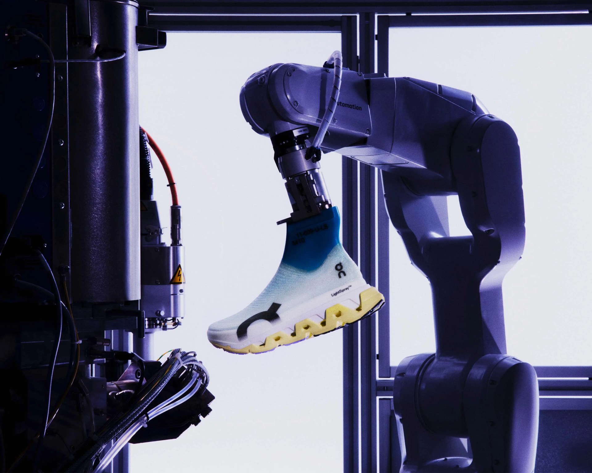 Robotic arm holding a white and blue sneaker with a yellow sole inside a manufacturing machine.