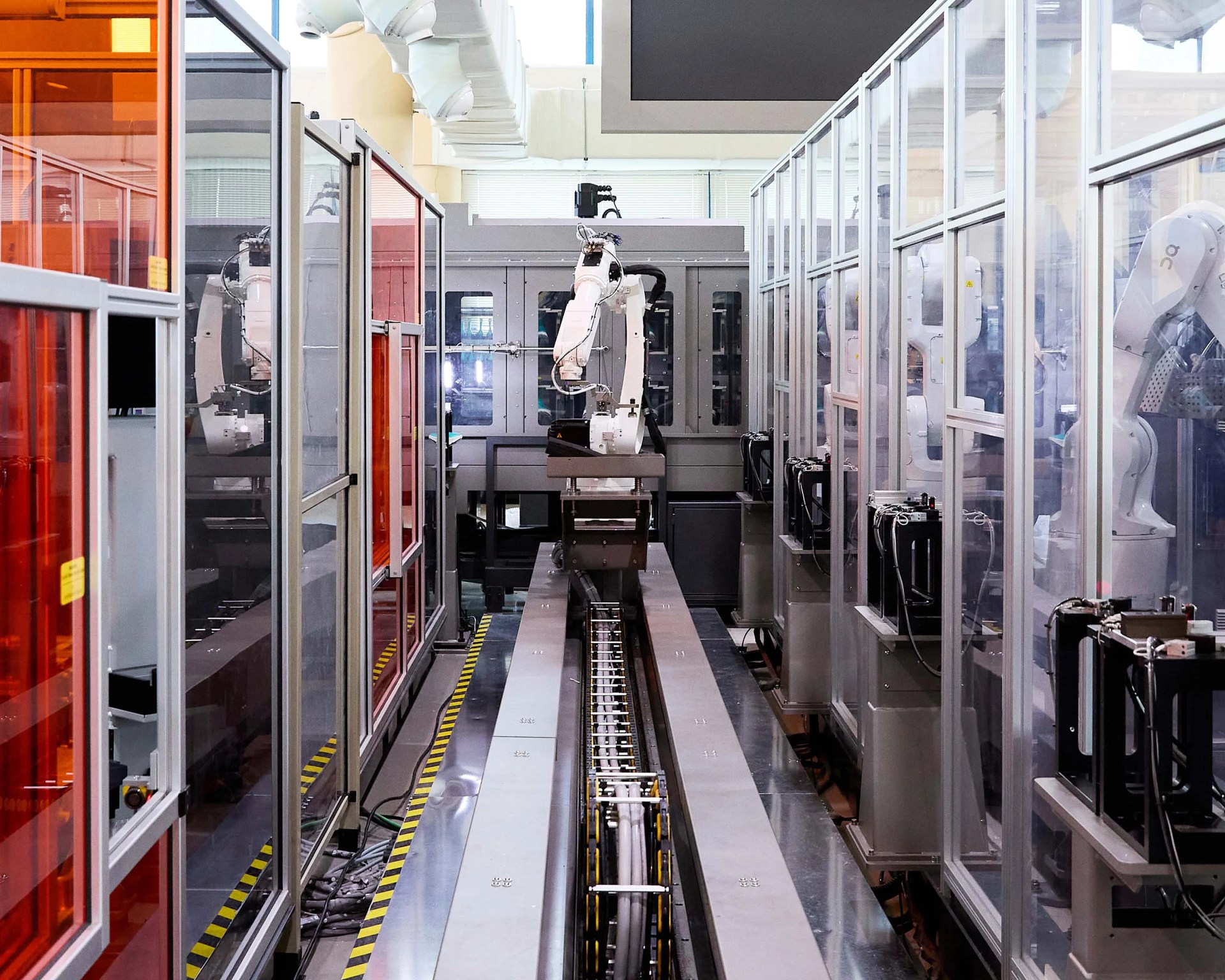 Robotic arm inside a glass-enclosed automated manufacturing line with metal conveyor belt.