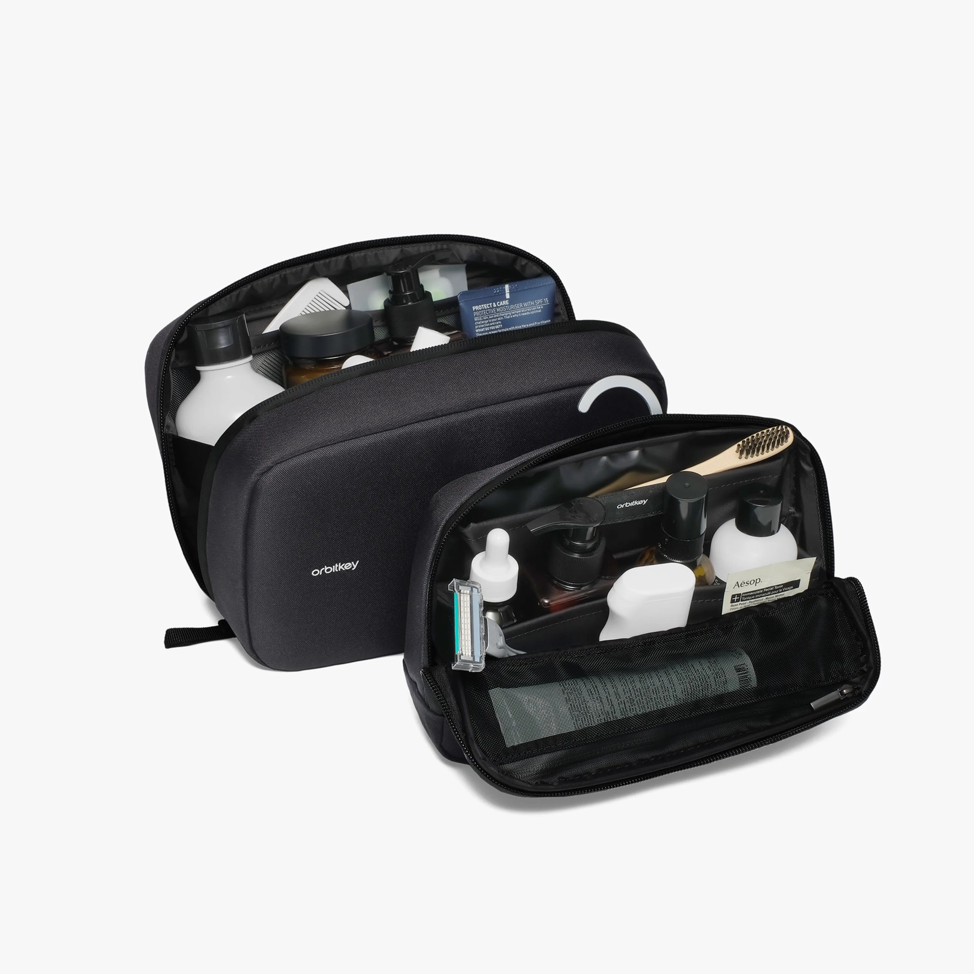 Two black Orbitkey toiletry bags open and filled with various travel-sized personal care items.