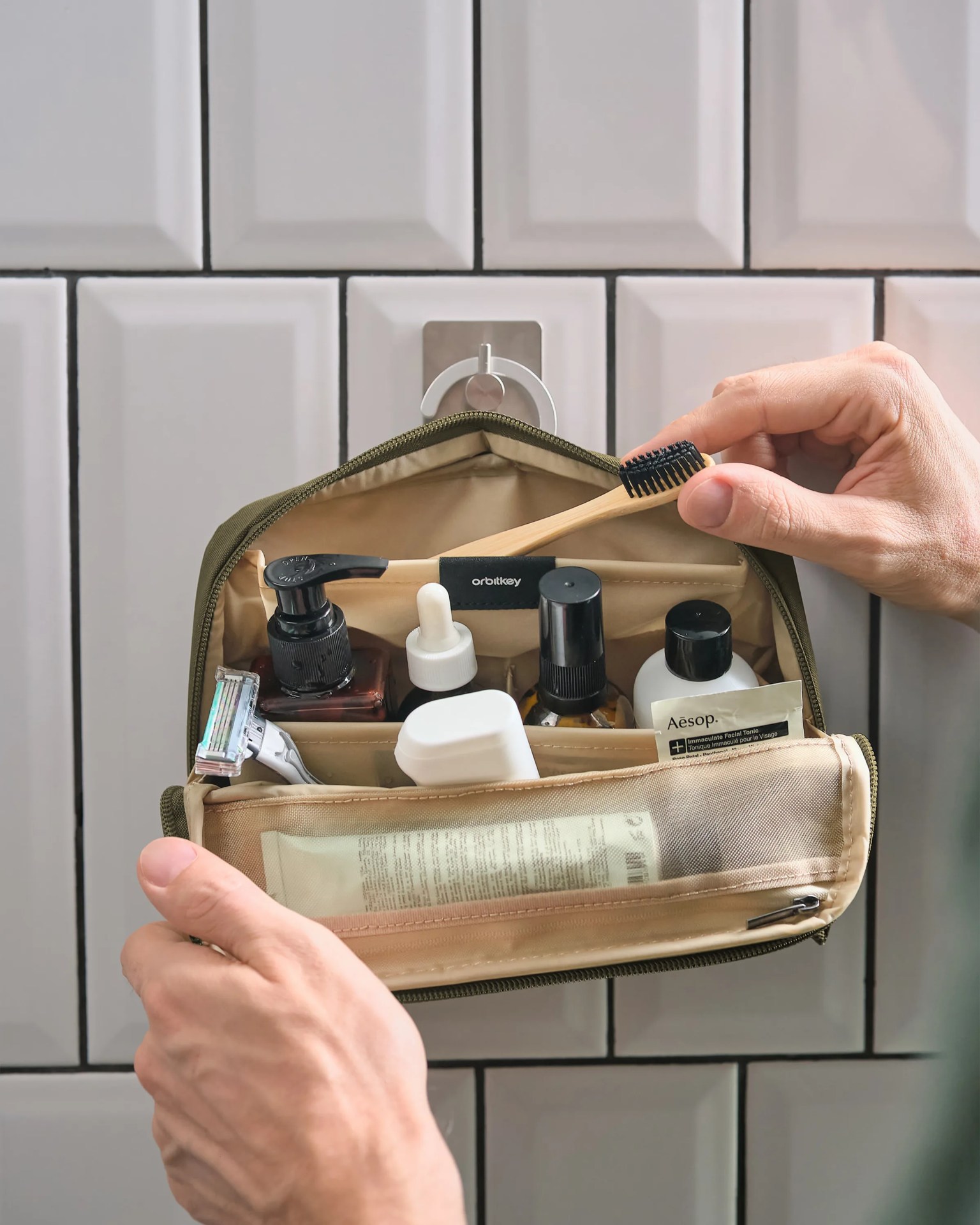 Olive-green hanging toiletry bag with compartments holding grooming products and a bamboo toothbrush.