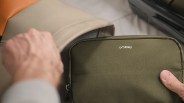 Olive-green fabric pouch with "orbitkey" logo held near a beige bag and black suitcase.