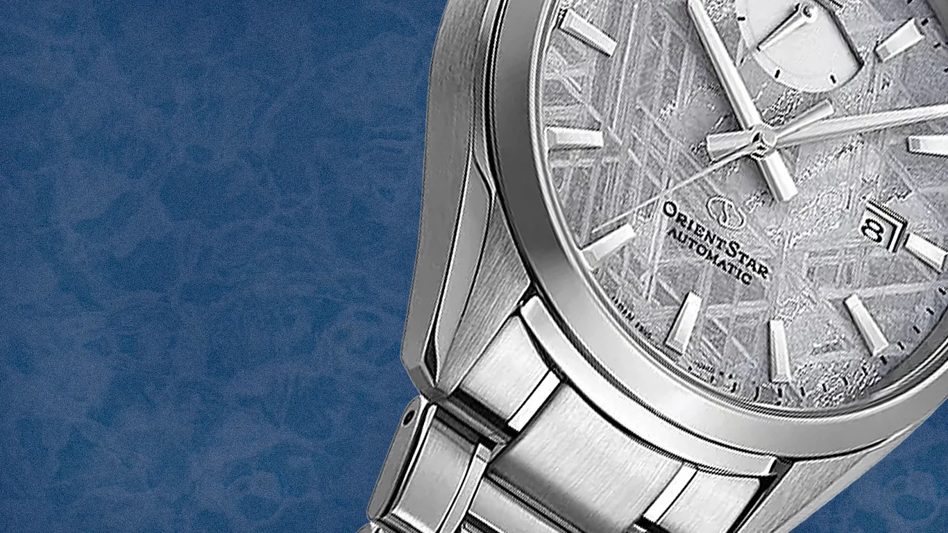 Silver stainless steel Orient Star automatic wristwatch with textured dial and date window on blue patterned background.