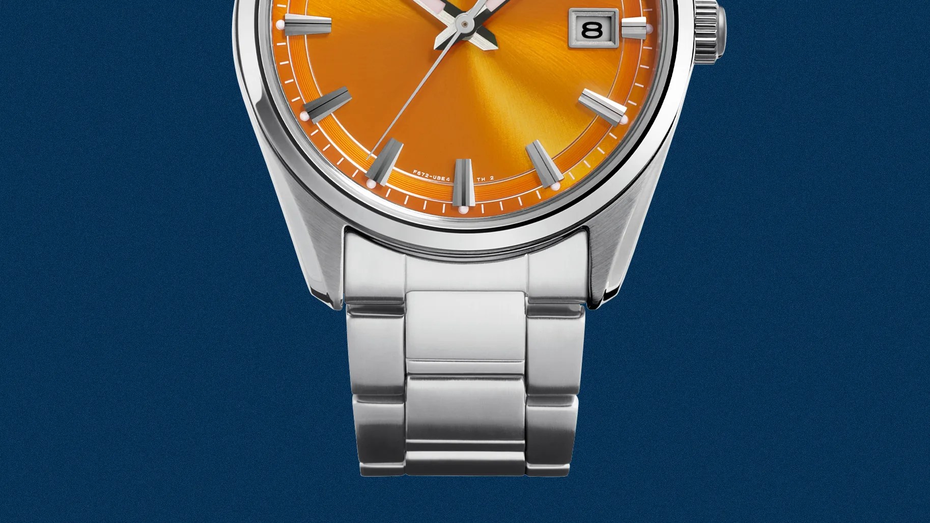 Close-up of a silver metal watch bracelet attached to a watch with an orange dial and date window.