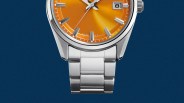 Close-up of a silver metal watch bracelet attached to a watch with an orange dial and date window.